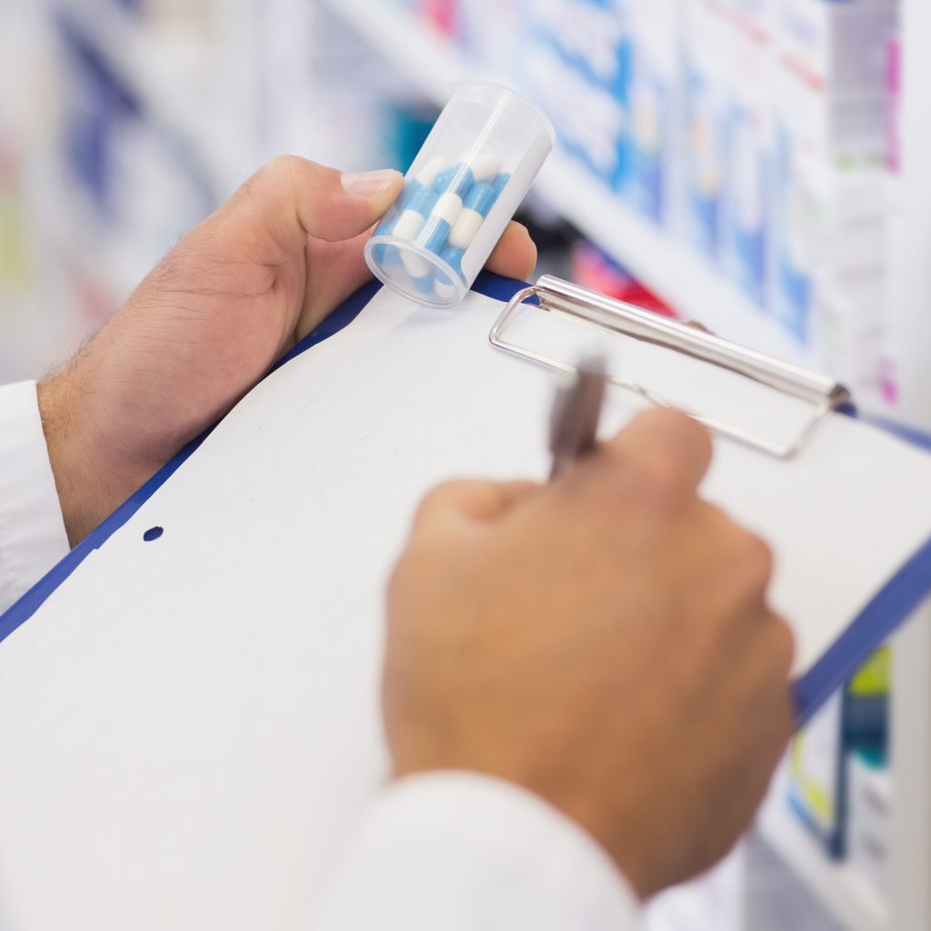 Pharmacist consulting a smiling customer in a modern pharmacy, with clipboard and medication visuals representing pharmacy vision in Alberta.