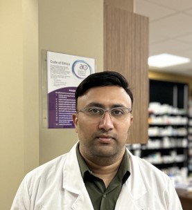 Chirag Bhatt, Board Director at Alberta Independent Pharmacy Association, standing in a pharmacy with shelves in the background.